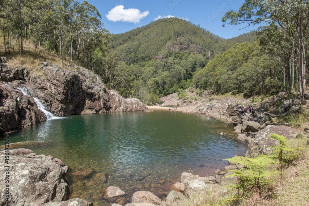 Tranquil waterfall pool nestled in a valley. Rocky shores, lush greenery, and a clear pool Tranquil waterfall pool nestled in a valley. Rocky shores, lush greenery, and a clear pool