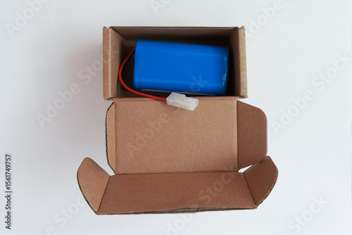 Blue battery with wire for household appliances in an open cardboard box on a white background.