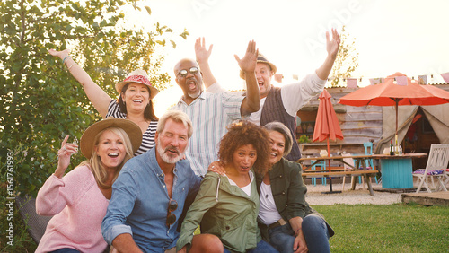 Portrait Of Mature Friends Sitting At Outdoor Campsite Bar Against Flaring Sun