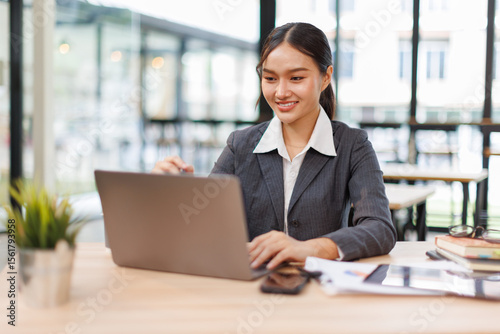 Young asian business woman sitting at the office and using laptops for document work. Confident professional female wearing business casual
