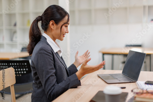 Excited friendly young asian woman 20s in casual clothes sit on desk,  talk work on laptop pc computer get video call gesticulate in living room at workplace.
