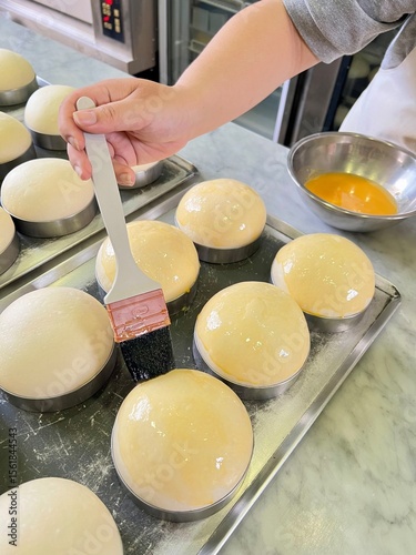 Close-up of a young woman's hand brushing butter or egg on dough while preparing to bake bread and burgers.