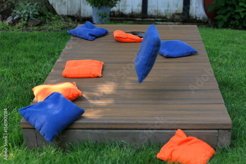 Blue cornhole bag in midair, about to join orange bags on a cornhole board