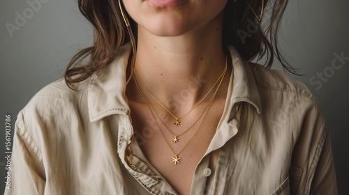 A woman posed on a gray background wears a beige shirt and a double gold necklace with star pendants. The necklace has two different chains.