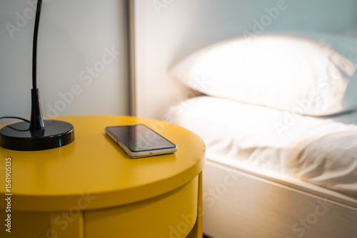 Smartphone lays on a bedside table in a bedroom before bedtime.