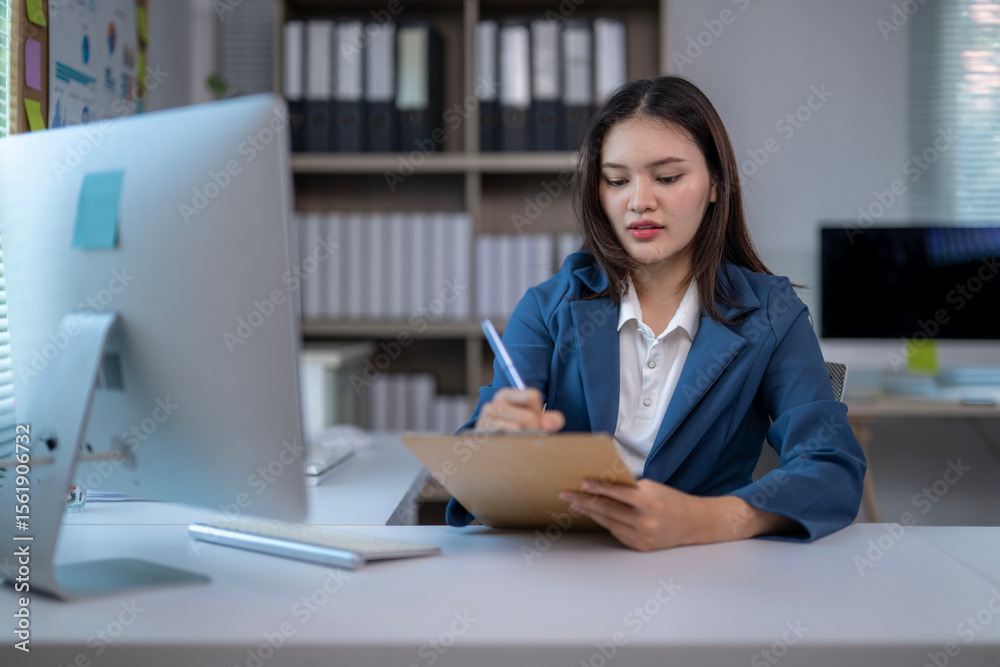 A woman is sitting at a desk with a computer monitor and a piece of paper A woman is sitting at a desk with a computer monitor and a piece of paper