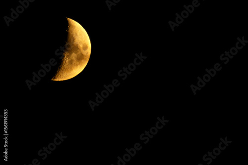 Close-up photo of a golden waxing half moon against a dark night sky, showing craters and lunar surface detail. Ideal for astronomy, science, or nature themes.