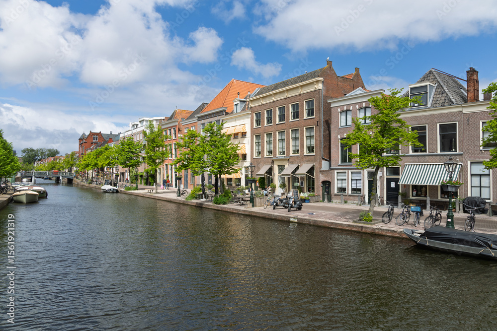 Fototapeta premium Beautiful canal scene in Leiden, Netherlands, featuring historic gabled houses, tree-lined quays, and a tranquil waterway. Perfect for travel, European architecture, and Dutch culture themes.