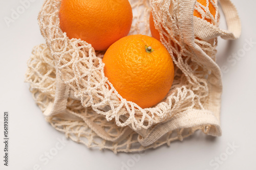Ripe juicy oranges in cotton string bag on light gray background top view flat lay. Eco-friendly thread bag for shopping, buying food, fruits, vegetables. Zero waste, plastic free concept 
