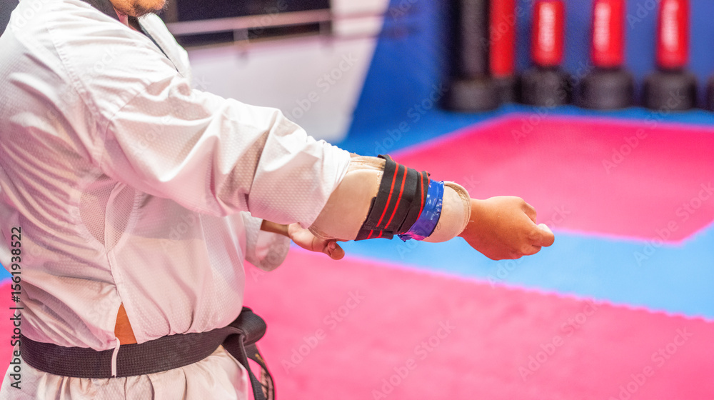Obraz premium Close-up of a martial arts practitioner adjusting an arm guard over his white uniform. The person is wearing a black belt, indicative of advanced level.