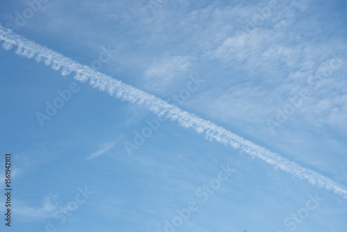 A clear blue sky with soft clouds and distinct plane tracks streaking across, creating a minimalist yet dynamic composition. A serene and airy view of the open sky.