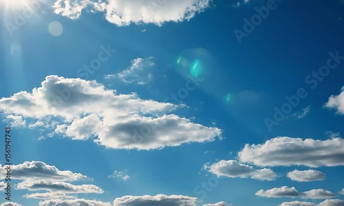 White Fluffy Clouds Against A Vibrant Blue Sky Illuminated By The Sun With Lens Flare