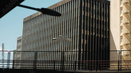 Modern cityscape with a tall glass office building, metal fencing and a speeding car on an overpass — showcasing urban density, architecture, infrastructure, transportation, and city life, facade