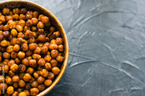 Delicious snack, fragrant baked with spices chickpeas in a brown bowl on a dark background with space for text. Healthy eating concept.