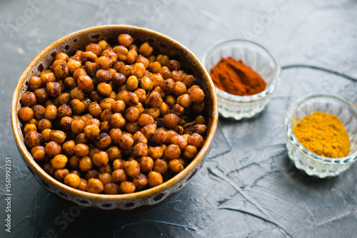 Delicious snack, fragrant baked with curry spices and smoked paprika chickpeas in a brown bowl and spices on a dark background with space for text. Healthy eating concept.