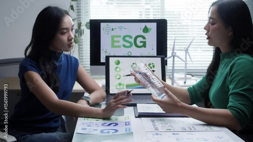 Professional Asian businesswomen working together, analyzing ESG sustainability data on laptop and tablet while discussing corporate environmental and social strategies