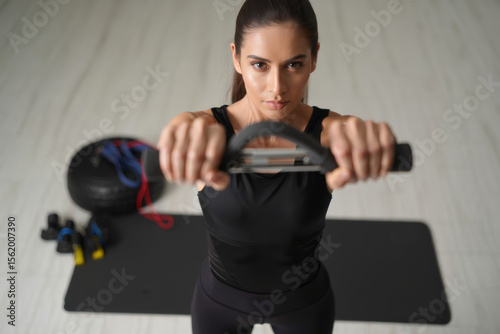 A fit American woman in black workout clothes demonstrates exercises while maintaining eye contact with the camera in her home gym.