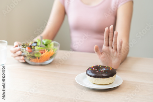 Φωτογραφία Diet, dieting, happy asian young woman, girl hand push out, deny sweet donut, doughnut on plate, choose tomato on fork and vegetable salad bowl, eat food for good healthy, female getting weight loss
