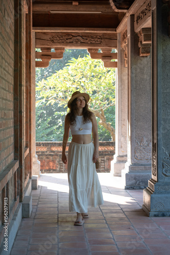 Young woman with straw hat and white dress visiting Temple of Literature in Hanoi, Vietnam, ancient university landmark