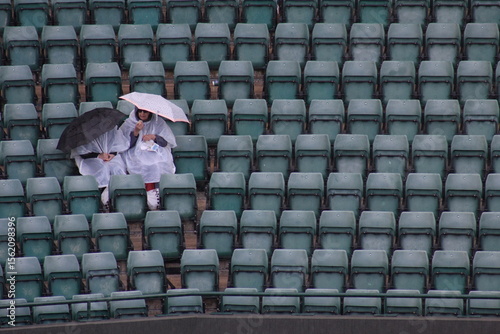 Photography Two people sit alone with umbrellas in seats at Wimbledon Centre Court after cov