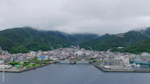 Flying over water to small coastal town by foggy mountains - Setouchi, Amami Island, Japan