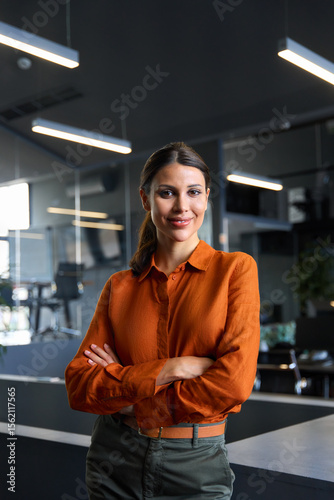 Vertical portrait of successful hispanic young business woman, saleswoman manager smiling at camera. Confident latin executive female leader professional businesswoman standing crossed arms in office