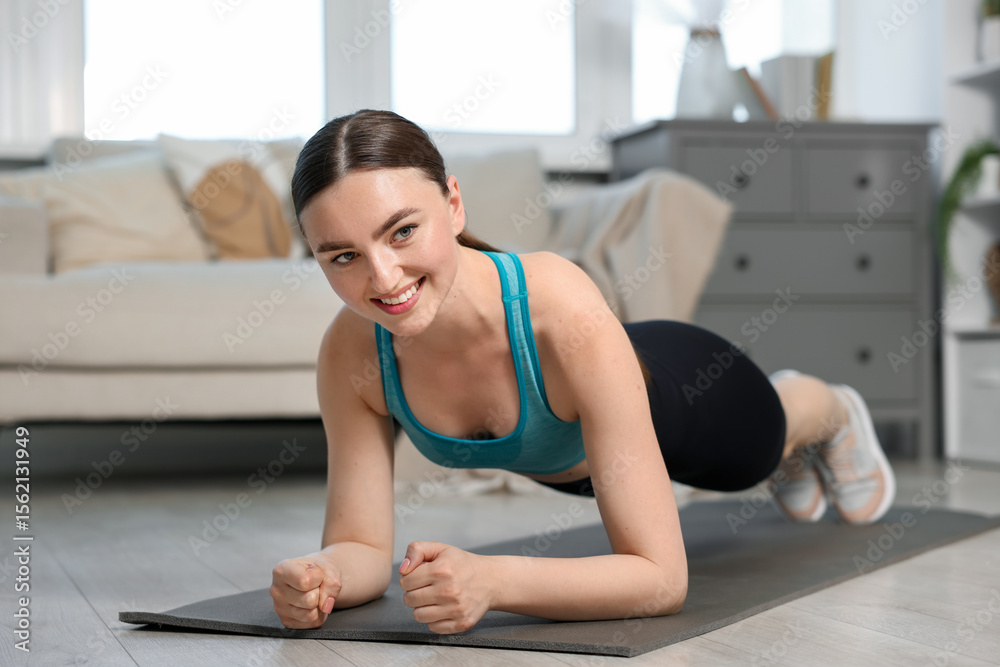 Obraz premium Smiling woman in sportswear doing plank exercise at home