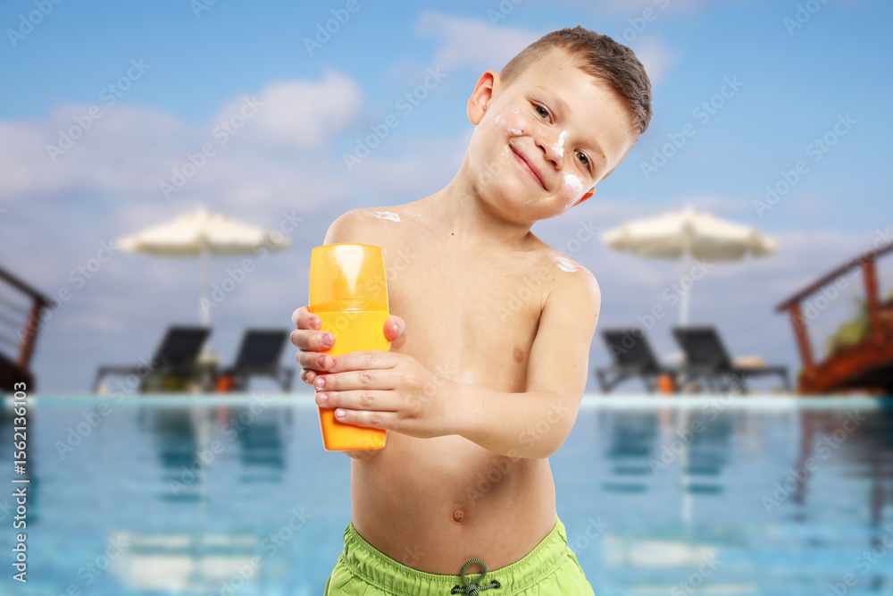 Little boy with bottle of sunscreen by outdoor swimming pool. Sun protection product on his skin Little boy with bottle of sunscreen by outdoor swimming pool. Sun protection product on his skin