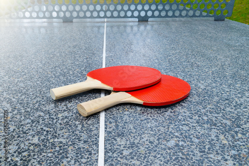 Red table tennis paddles on outdoor stone ping pong table