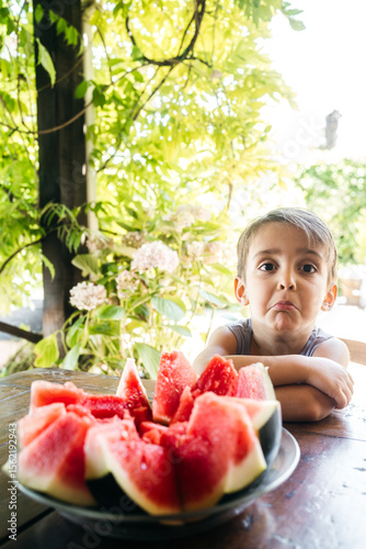 Child Eating Watermelon with Displeased Expression at Garden Table — Real Moment in Healthy Eating Exploration