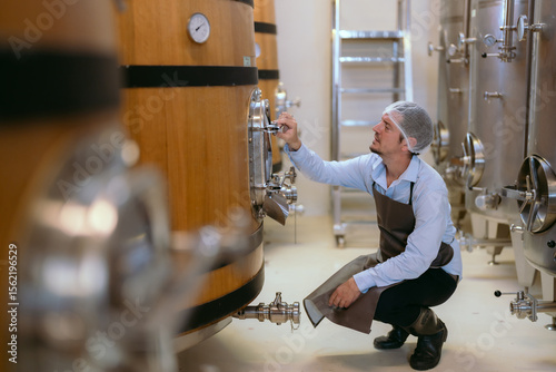 Winery worker inspecting fermentation tanks in a modern facility during daytime
