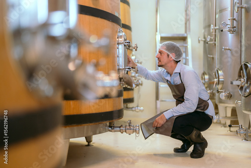Winery worker inspecting fermentation tanks in a modern facility during daytime