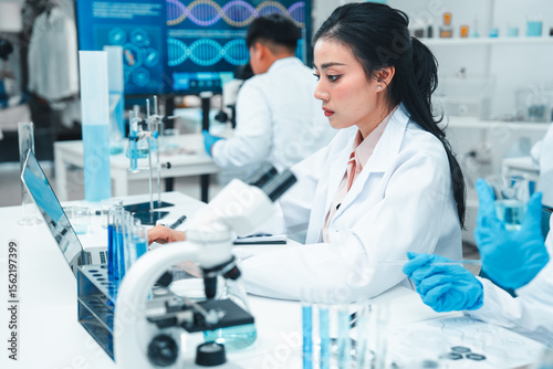 Two female scientists analyzing test tube samples in a laboratory setting. One supervises while the other conducts an experiment. Concept of science education, teamwork, and research collaboration.
