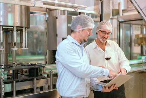 Two professionals discuss quality control in a food processing plant during working hours while reviewing data on a laptop