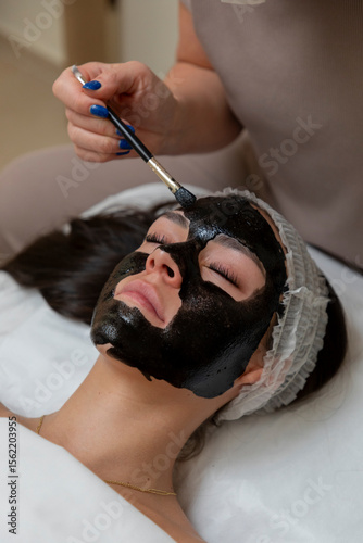 Tableau sur toile Beautician applying black mask treatment to woman's face in spa