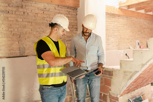 Contractor and engineer using laptop discussing project details during building construction
