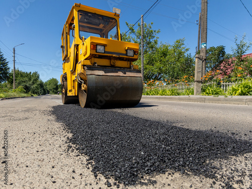 A road roller is laying asphalt on the side of the road