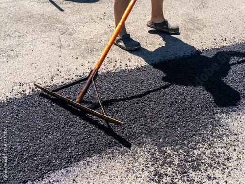 A man is using a rake to clean the asphalt of a parking lot