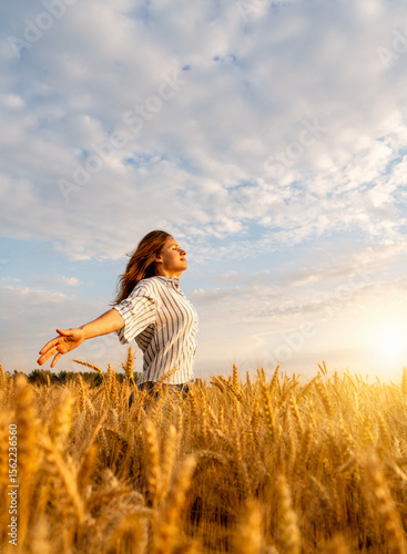 Proud woman with outstretched arms standing in cereal field in countryside during golden hour