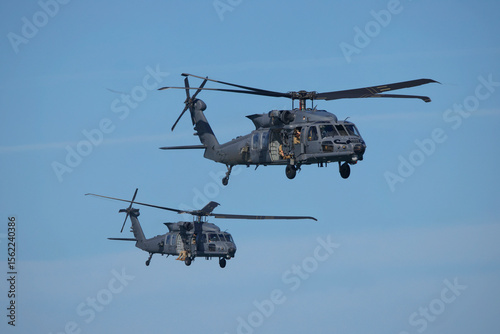 Two military Blackhawk helicopters flying in formation on clear blue sky. 