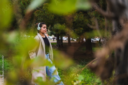Young stylish influencer walking in a park listening to music with wireless headphones