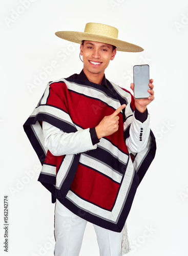 Happy chilean huaso wearing traditional poncho and hat pointing at smartphone with blank screen, Fiestas Patrias celebration