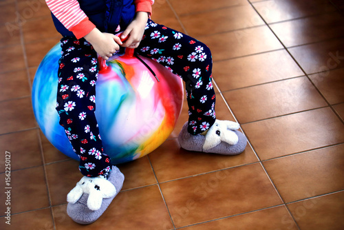 Child sitting on colorful jumping ball wearing bunny slippers