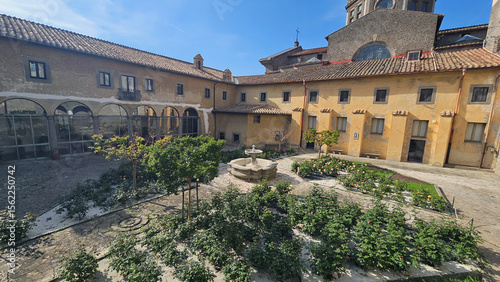 Schilderij op canvas Cloister Garden with Fountain and Rose Bushes