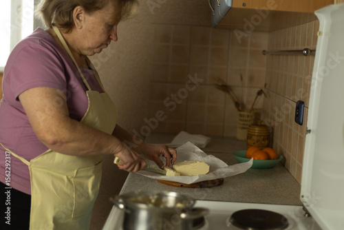 Senior woman additionally cuts sweet butter into a pan to melt, preparing ghee butter