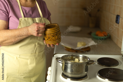 The hands of a senior woman add salt to sweet butter on the stove