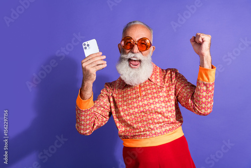 Obraz na plátně Cheerful senior man in retro fashion attire holding smartphone against vibrant p