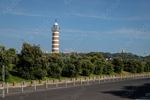 The striped Belem Lighthouse stands tall near Lisbon, Portugal, under clear blue skies on a quiet summer afternoon, guiding vessels navigating the Tagus River's entrance.
