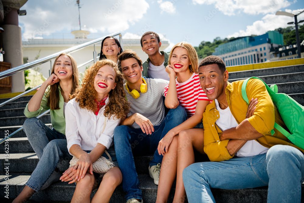 Obraz premium Group of joyful young friends relaxing on urban steps during a sunny day, enjoying summer, bonding