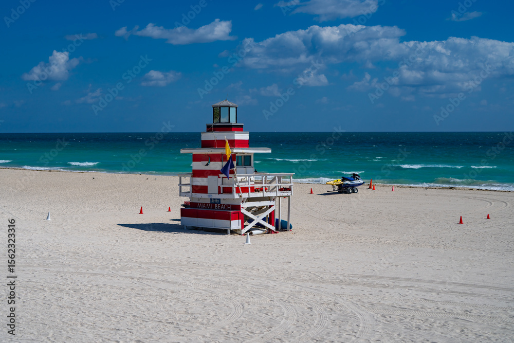 Obraz premium Miami Beach lifeguard at the summer beach. South Miami Beach with lifeguard. Sky above lifeguard tower in Miami. Iconic lifeguard tower on sand in Miami. A symbol of Miamis coast.